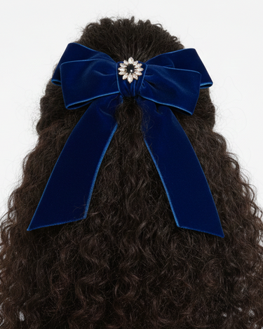 Blue velvet hair bow on curly hair against a white background