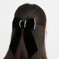 Black hair bow with pearl details on a person's hair against a white background
