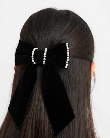 Black hair bow with pearl details on a person's hair against a white background