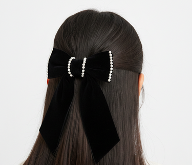 Black hair bow with pearl details on a person's hair against a white background