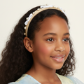 Young girl wearing a headband with pearls and a bow on a plain background