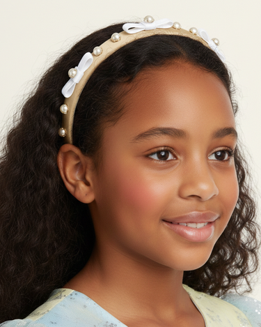 Young girl wearing a headband with pearls and a bow on a plain background