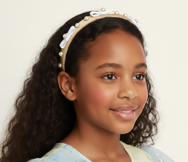 Young girl wearing a headband with pearls and a bow on a plain background