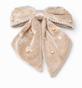 Beige velvet bow with pearl embellishments on a white background
