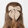 Beige bow hair clip with pearls on a person's head against a white background