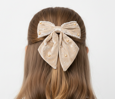 Beige bow hair clip with pearls on a person's head against a white background