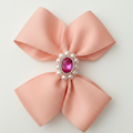 Pink bow with a central gemstone and pearls on a light gray background