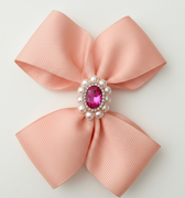Pink bow with a central gemstone and pearls on a light gray background