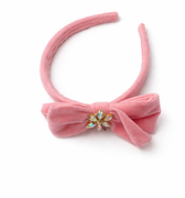 Pink velvet bow headband with a decorative center on a white background
