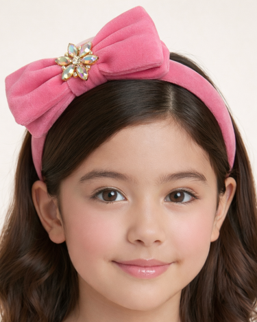 Young girl wearing a pink headband with a decorative bow on a plain background