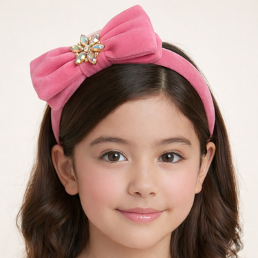 Young girl wearing a pink headband with a decorative bow on a plain background