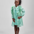 Girl in mint glitter jersey dress with silk organza overshirt and feather trim.