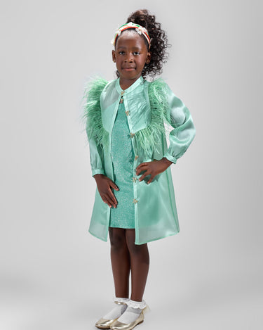 Girl in mint glitter jersey dress with silk organza overshirt and feather trim.