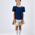 Girl in navy velvet and floral brocade dress with puff sleeves and scalloped detail.