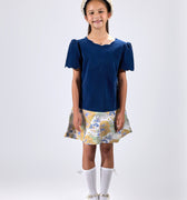 Girl in navy velvet and floral brocade dress with puff sleeves and scalloped detail.