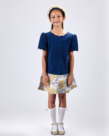 Girl in navy velvet and floral brocade dress with puff sleeves and scalloped detail.