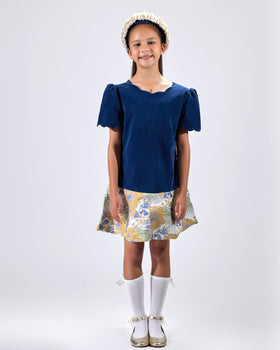 Girl in navy velvet and floral brocade dress with puff sleeves and scalloped detail.