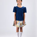 Girl in navy velvet and floral brocade dress with puff sleeves and scalloped detail.