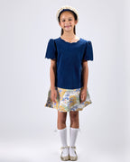 Girl in navy velvet and floral brocade dress with puff sleeves and scalloped detail.