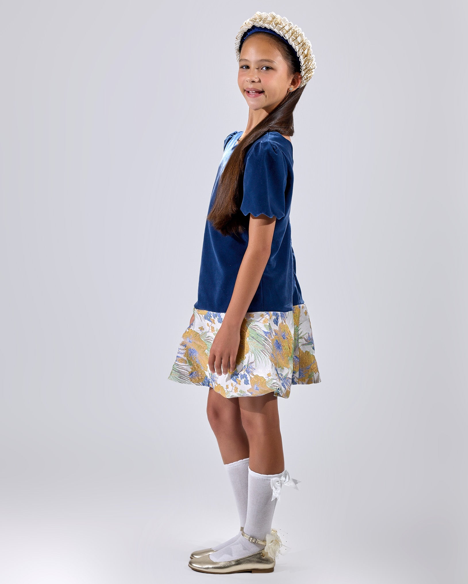 Girl in navy velvet and floral brocade dress with puff sleeves and scalloped detail.