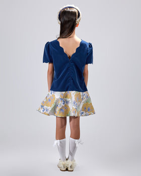 Girl in navy velvet and floral brocade dress with puff sleeves and scalloped detail.