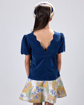Girl in navy velvet and floral brocade dress with puff sleeves and scalloped detail.