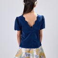 Girl in navy velvet and floral brocade dress with puff sleeves and scalloped detail.