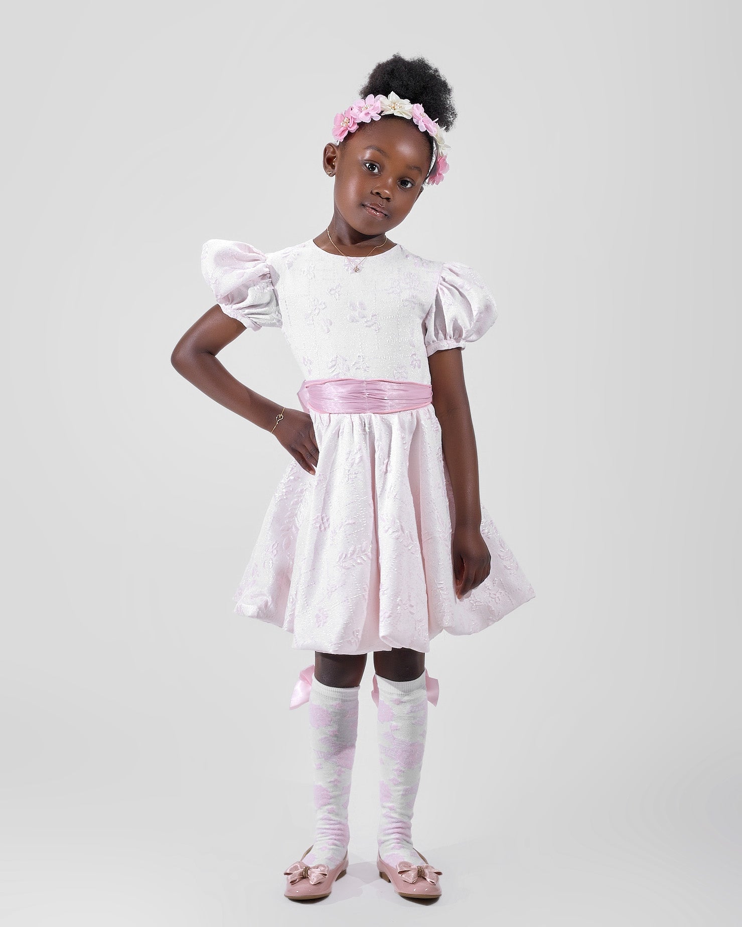 Girl in blush pink floral brocade dress with puff sleeves and organza bow.