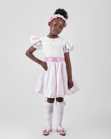 Girl in blush pink floral brocade dress with puff sleeves and organza bow.