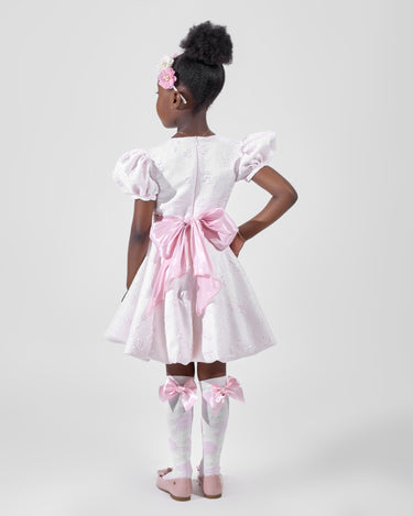 Girl in blush pink floral brocade dress with puff sleeves and organza bow.