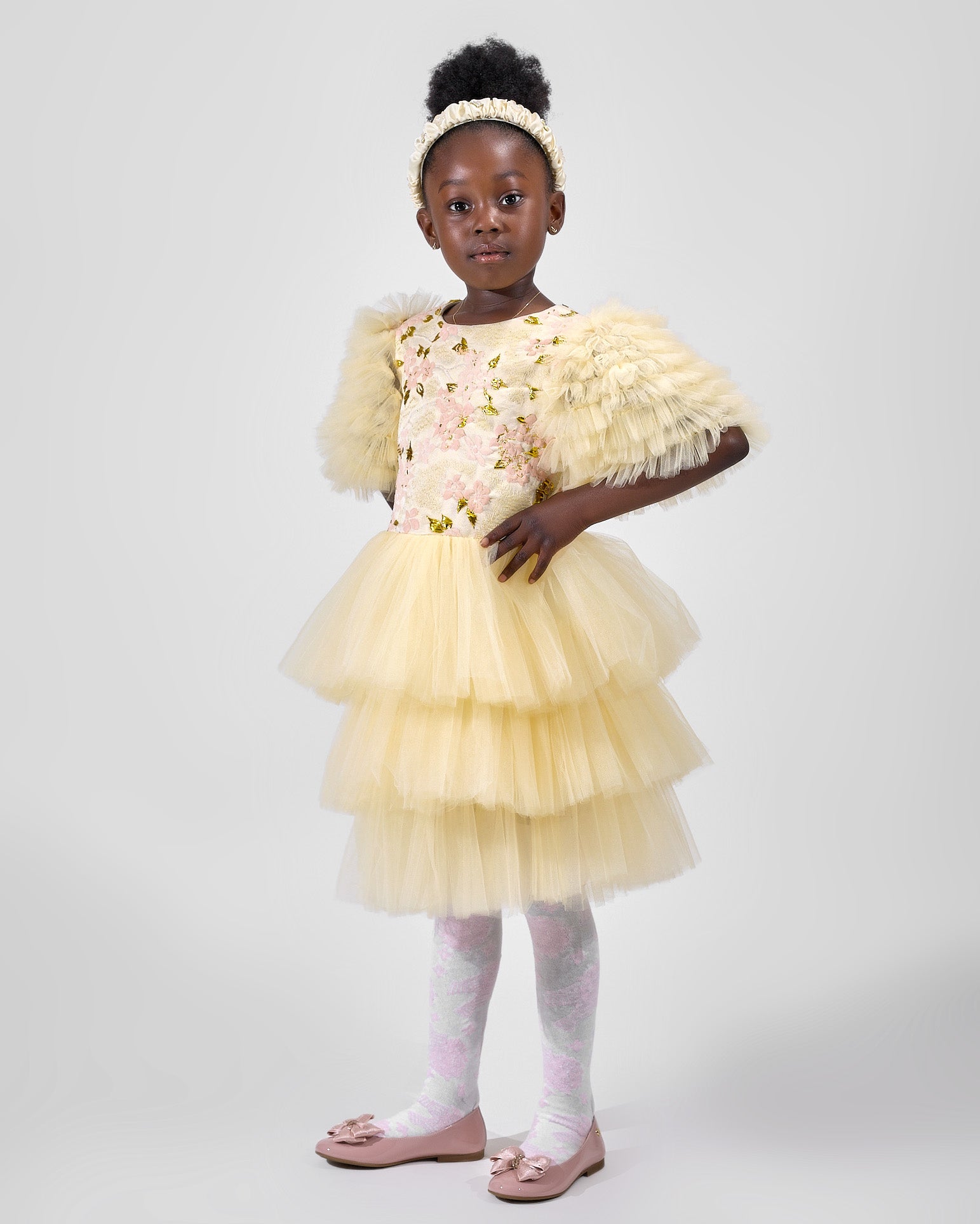 Young girl wearing a yellow dress with floral details and a matching shawl on a white background
