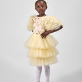 Young girl wearing a yellow dress with floral details and a matching shawl on a white background