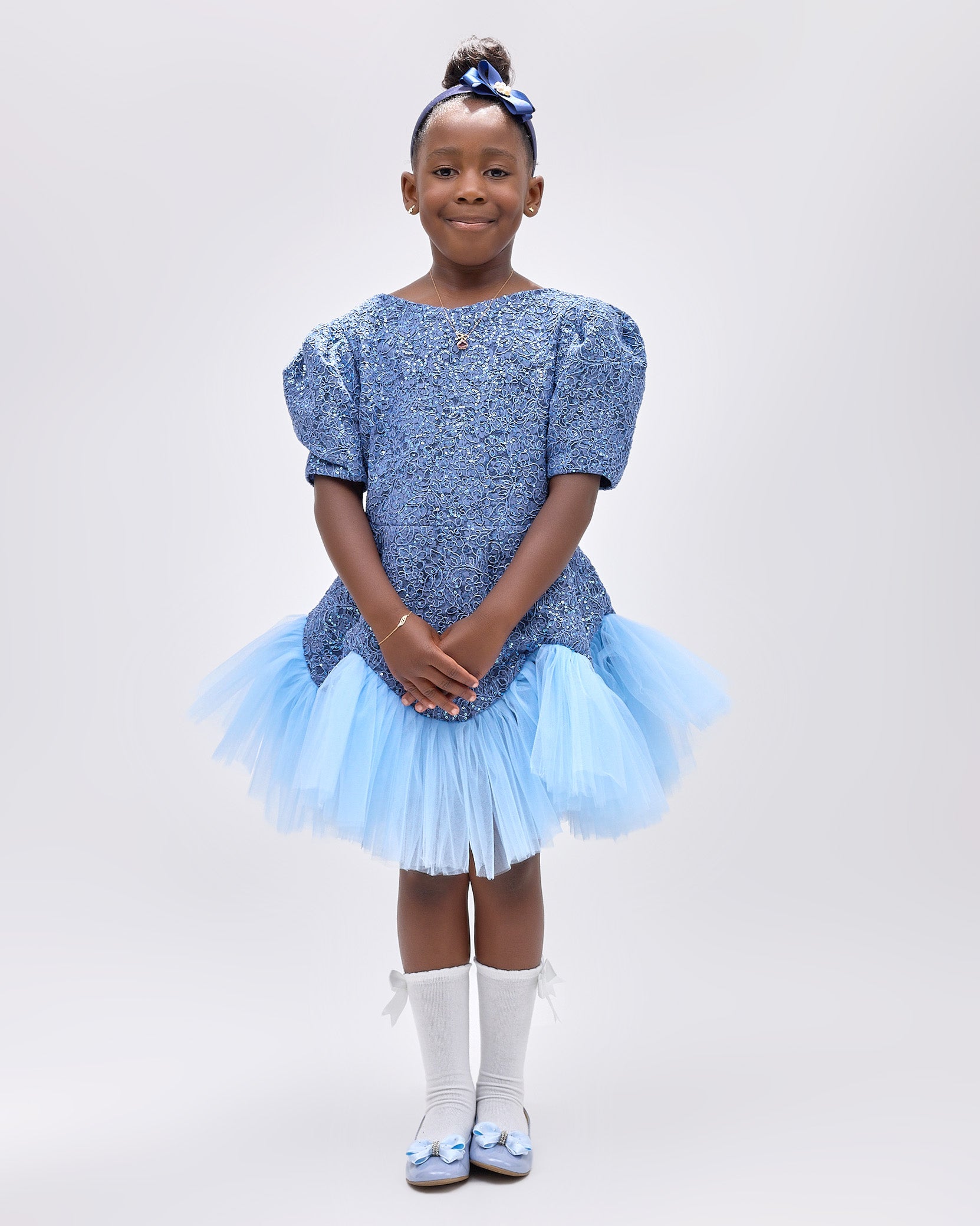 Girl wearing soft blue embroidered lace dress with puff sleeves and tulle hem.