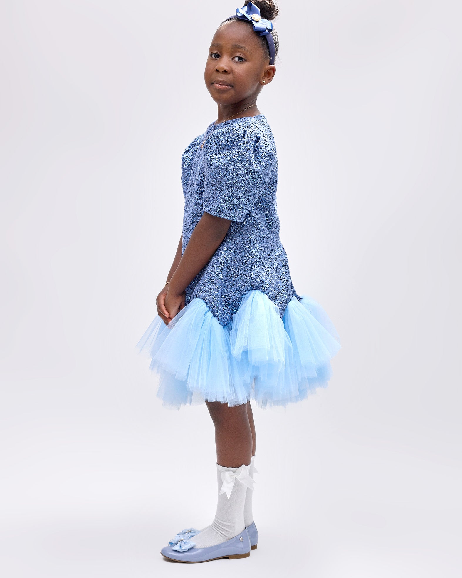 Girl wearing soft blue embroidered lace dress with puff sleeves and tulle hem.