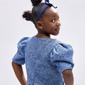 Girl wearing soft blue embroidered lace dress with puff sleeves and tulle hem.