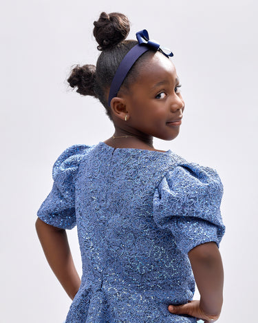 Girl wearing soft blue embroidered lace dress with puff sleeves and tulle hem.
