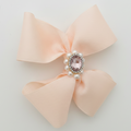 Pink bow with a central gemstone and pearls on a light gray background