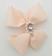 Pink bow with a central gemstone and pearls on a light gray background