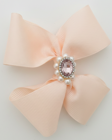 Pink bow with a central gemstone and pearls on a light gray background