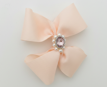 Pink bow with a central gemstone and pearls on a light gray background