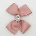 Pink bow with a central gemstone and pearls on a light gray background