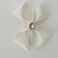 Cream-colored bow with a pink gem and pearl center on a light gray background