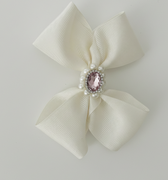 Cream-colored bow with a pink gem and pearl center on a light gray background