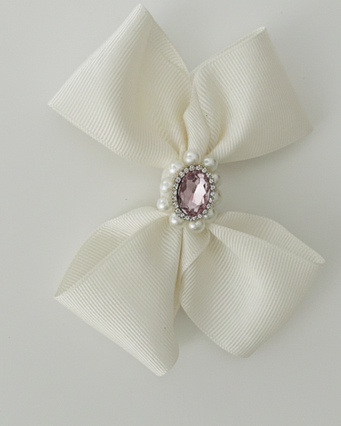 Cream-colored bow with a pink gem and pearl center on a light gray background