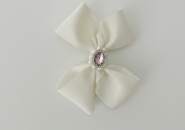 Cream-colored bow with a pink gem and pearl center on a light gray background