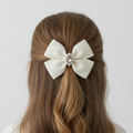White hair bow with a central gemstone on brown hair against a white background