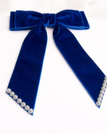 Blue velvet bow with pearl accents on a white background