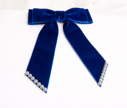 Blue velvet bow with pearl accents on a white background