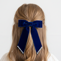 Navy blue velvet hair bow with pearl accents on a person's head against a white background