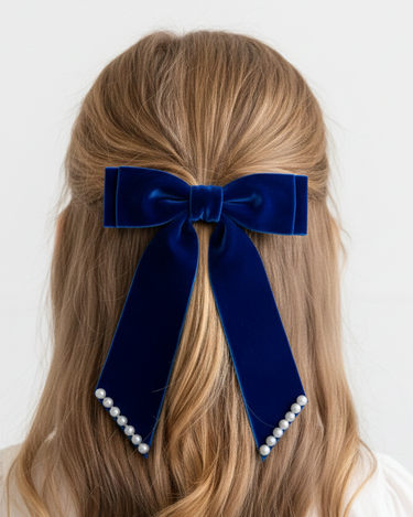 Navy blue velvet hair bow with pearl accents on a person's head against a white background